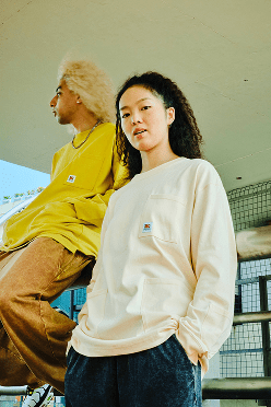 Girl wearing yellow top looking into distance with girl in front of her wearing white top looking at camera