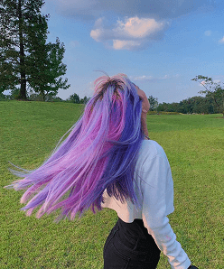 Girl with purple and blue hair turning around in nature background