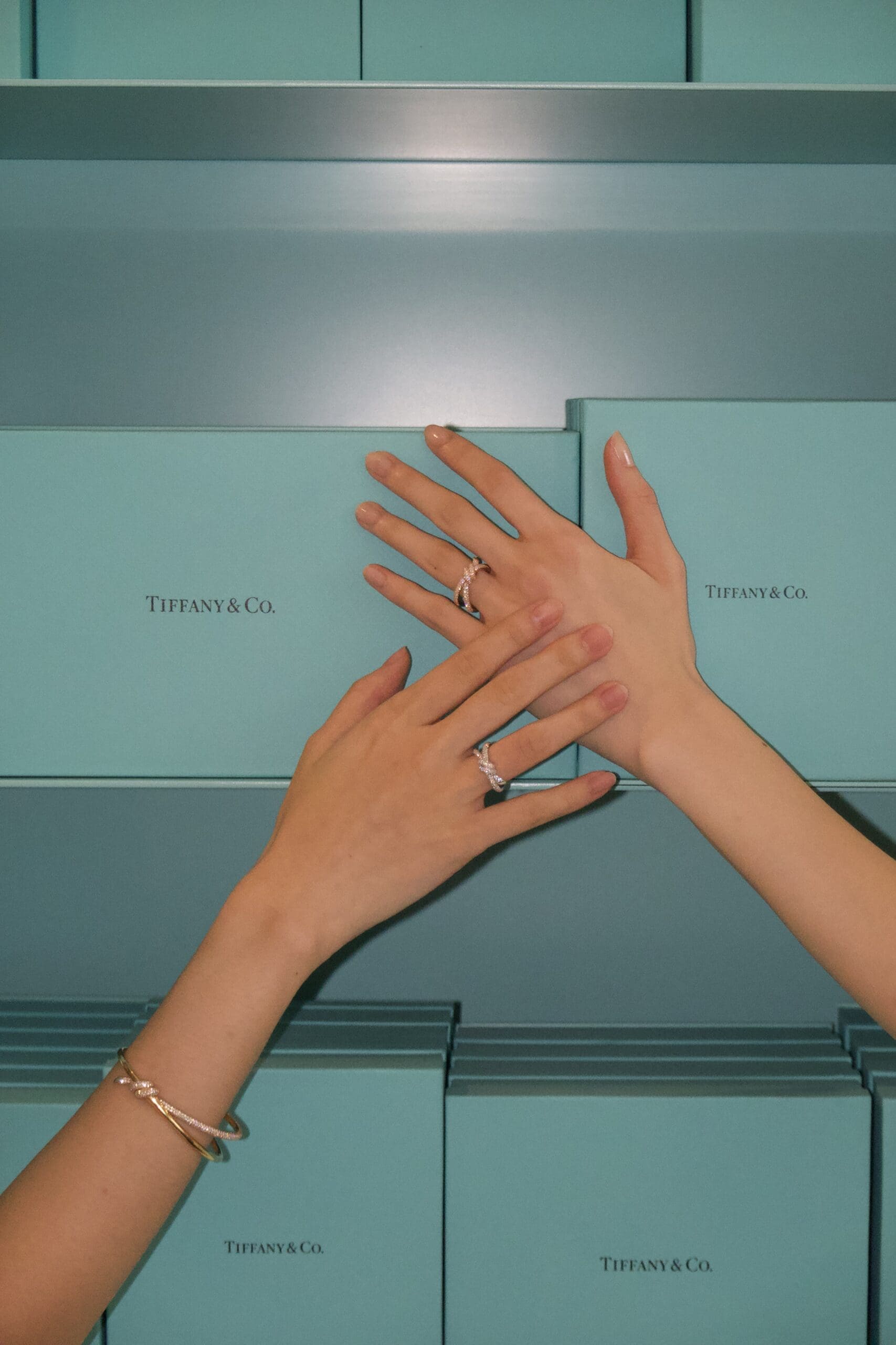 Two female hands wearing Tiffany and Co's luxury jewellery on a background of torquose Tiffany boxes