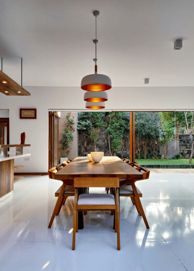 Large brown dining room table in the middle or a spacious dining room with sliding window doors and white marble floors